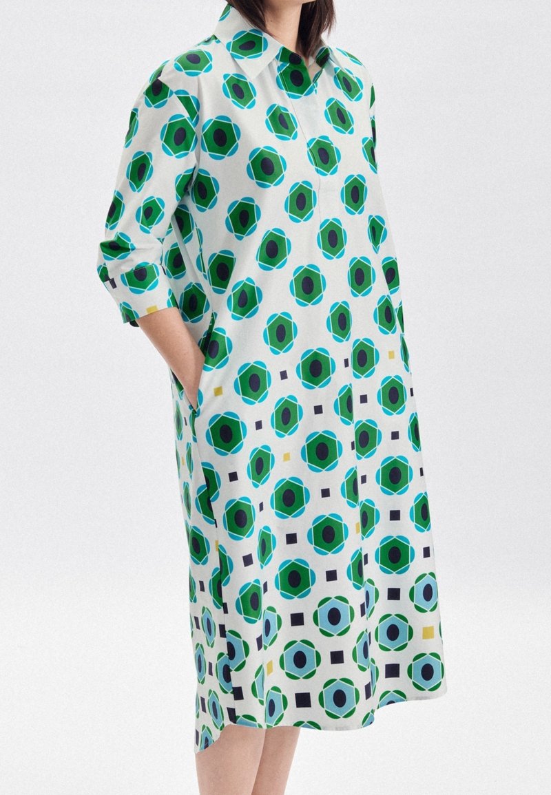 Vestito a maniche corte in tessuto leggero, caratterizzato da un audace motivo geometrico nei colori verde, blu, nero e bianco. Include tasche laterali.