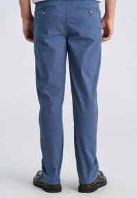 Pantaloni in cotone azzurro con vestibilità rilassata, due tasche posteriori e dettagli con bottoni, abbinati a scarpe nere.