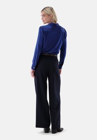 Satin blue long-sleeve shirt with a classic collar, paired with high-waisted, wide-leg black trousers and heeled ankle boots.