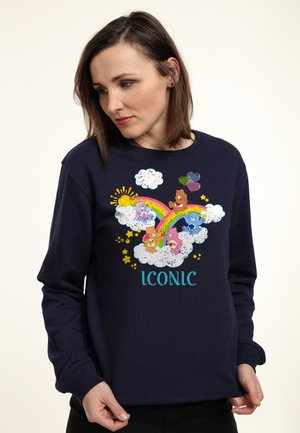 Marineblå sweatshirt med et farverigt grafik af bjørne, en regnbue og skyer, med ordet "ICONIC" i turkis. Lange ærmer og rund hals.
