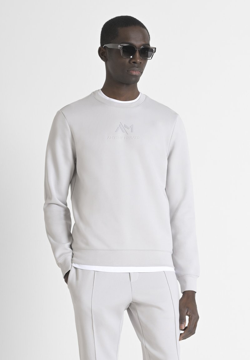 Lichtgrijze sweatshirt met ronde hals en geribbelde manchetten, met een 3D-logo aan de voorkant. Gecombineerd met bijpassende lichtgrijze broek.