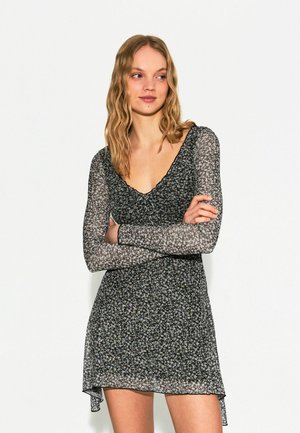 Black floral dress made from sheer fabric, featuring long sleeves, a V-neckline, and a ruffled trim with a slightly flared hemline.