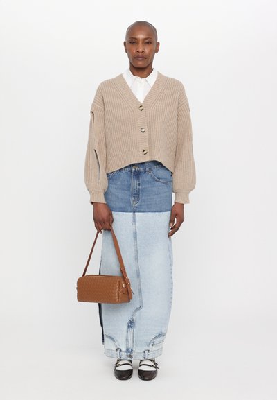 Beige knitted cardigan, cropped with buttons; blue denim skirt, long with a gradient; brown woven handbag; black and white shoes.