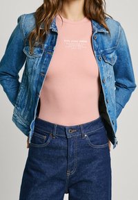 Denim jacket with light blue wash, fitted pink ribbed t-shirt, and dark blue jeans with orange stitching and button closure.