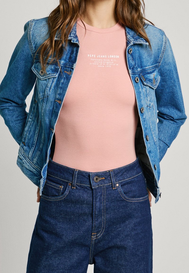 Denim jacket with light blue wash, fitted pink ribbed t-shirt, and dark blue jeans with orange stitching and button closure.