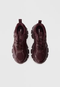 Burgundské športové tenisky s vrchnou časťou z sieťoviny a syntetického materiálu, hrubou gumovou podrážkou, polstrovaným golierom a šnurovaním. Štruktúrované detaily na bokoch.