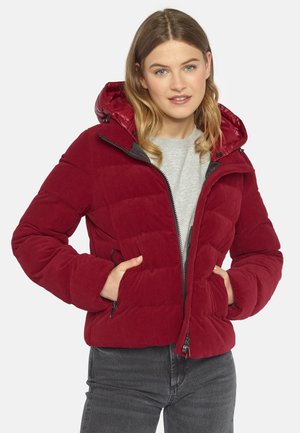 Rote Cordjacke mit Kapuze, verfügt über ein gestepptes Design, einen Reißverschluss vorne und Seitentaschen. Getragen über einem grauen Shirt.