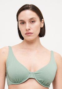 Bra verde a coste con un classico design con ferretto, dotato di spalline larghe e una cucitura centrale. Texture liscia e vestibilità su misura.