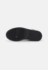 Schwarze Sneakersohle aus strukturiertem Gummi, mit kreisförmigem Profilmuster und vertieften Rillen. Nike-Logo nahe der Ferse geprägt.