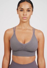 Sujeción deportiva gris con textura acanalada, diseño de escote en V y tirantes dobles finos. Presenta un detalle fruncido en la parte central delantera.