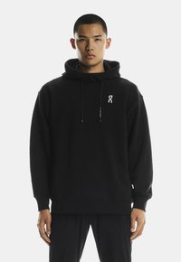 Juodas gobtuvų džemperis su laisvu kirpimu, ant krūtinės yra baltas logotipas, su raišteliu reguliuojamu gobtuvu bei rebrastais rankogaliais ir apačia.