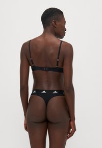 Black lingerie set featuring a bralette with adjustable straps and a hook closure, paired with a thong displaying a branded waistband.