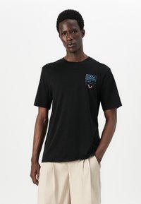 Black cotton t-shirt with short sleeves, featuring a blue embroidered logo on the chest. Simple design, soft texture, relaxed fit.