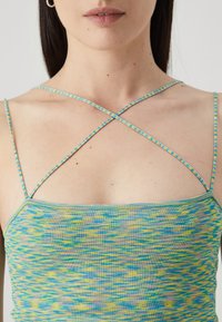 Multicolored tank top with a tight fit, featuring a crisscross strap design. Colors include blue, yellow, and green patterns on a textured fabric.