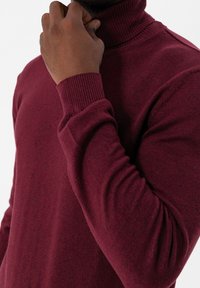 Suéter burdeos de cuello alto con puños y cuello acanalados. Textura de punto, diseño ajustado y detalles de patrón sutiles. Composición de tela suave.