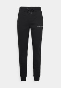 Černé tepláky vyrobené z měkké tkaniny, s elastickým pasem na stahování a žebrovanými manžetami. Logo "TOMMY HILFIGER" vytištěné bílou barvou na boku.