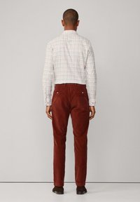 Witte geruite shirt met rode en blauwe lijnen, gecombineerd met bordeauxkleurige corduroy broek. De outfit wordt compleet gemaakt met donkerbruine schoenen.