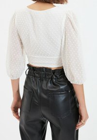 Cropped top a maniche puff con pois bianchi, realizzato in tessuto trasparente, abbinato a pantaloni neri in ecopelle a vita alta con tasche posteriori.