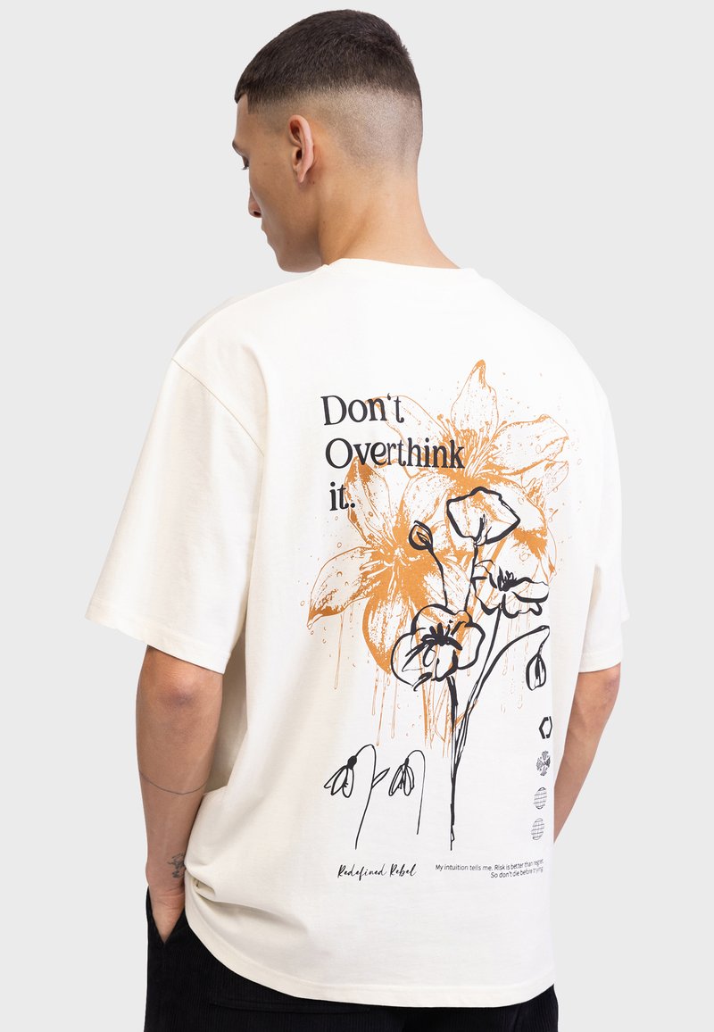 Roomkleurig T-shirt met korte mouwen met een oranje bloemenpatroon en zwarte tekst op de achterkant, een ontspannen pasvorm en een rechte zoom.