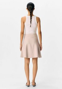 Un débardeur blanc associé à une jupe évasée d'un doux rose pâle. Le tissu semble lisse, avec un léger éclat. Design simple, longueur jusqu'aux genoux.