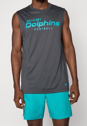 Mann trägt ärmelloses dunkelgraues Miami Dolphins Football-Trikot und türkisfarbene Sportshorts mit Nike-Logos vor einfarbigem Hintergrund.