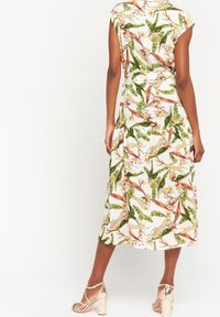 Sukienka w kwiatowy nadruk z krótkimi rękawami, z zielonymi liśćmi i pomarańczowymi kwiatami na białym tle. Średnia długość, zwiewny materiał, z paskiem w talii.
