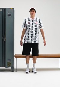 Men's short-sleeve jersey featuring a black and white geometric pattern with pink accents, paired with black shorts and white sneakers.