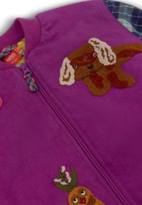 Paarse ritsvest met pluizige textuur, met geborduurde accenten van een bruine hond en een personage met groen. Kleurrijke ritsophang aan de nek.