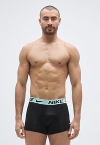 Sorte boxer briefs med en lyseblå Nike-mærket linning, med en glat tekstur og tætsiddende pasform, fremvist på en mandlig model.