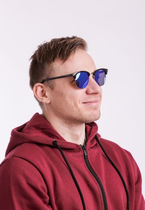 Round sunglasses with blue mirrored lenses, black frames, and a metallic accent. Worn by a person in a burgundy hoodie.