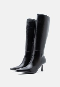 Μαύρες μπότες μέχρι το γόνατο, φτιαγμένες από γυαλιστερό δέρμα, με μυτερή μύτη, τακούνι στιλέτο και πλευρικό φερμουάρ για εύκολη φορεσιά.