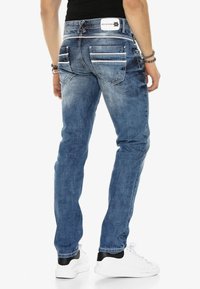 Jeans en denim bleu clair avec une coupe slim, dotés de plusieurs poches arrière, de coutures blanches et d'une étiquette de marque sur la ceinture.