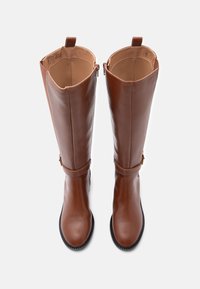 Barna bőr, térdfelett érő csizmák sima textúrával, lekerekített orral és kontrasztos fekete gumitalppal; oldalsó cipzárral és bokapántokkal.