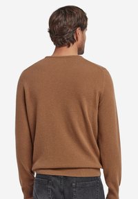 Brun tröja, lättviktsstickat tyg, rund halsringning, långa ärmar, ribbade muddar och fåll, slät textur, bärs med mörka jeans.