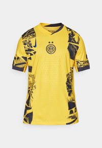 Kollane särg, millel on mustad abstraktsed mustrid, ümmargune kaelus, lühikesed varrukad ja keskel asuv logo kahe tähega selle kohal.