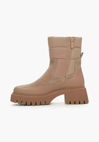 Beige enkelboot met een gequilt bovendeel, zijrits en een chunky, geribbeerde plateauzool. Gemaakt van Suède en synthetische materialen.