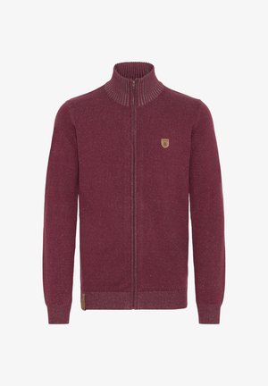 Bordeaux kleurige ritstrui met hoge kraag, geribbelde textuur en een klein logo op de borst. Beschikt over lange mouwen en een aansluitende pasvorm.