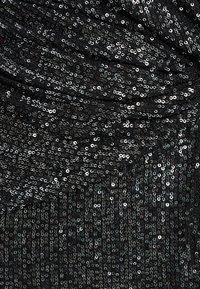 Gros plan sur un tissu noir densément recouvert de sequins argentés réfléchissants, montrant une texture froncée et drapée.