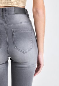 Grey high-waisted jeans with a faded finish, featuring two back pockets, a leather patch at the waistband, and a slim fit design.
