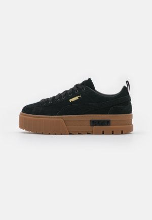 Czarny zamszowy sneaker Puma z grubą brązową podeszwą i złotym logo Puma z boku, widziany od zewnętrznej strony.