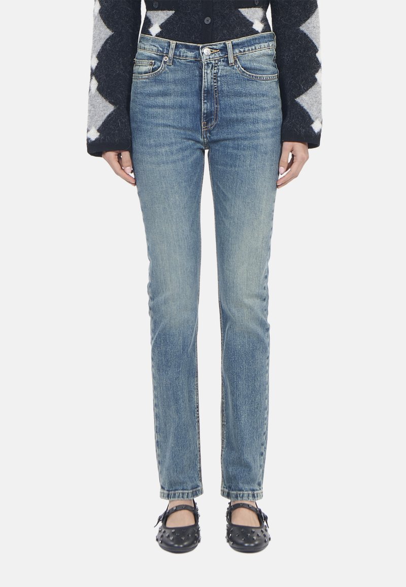 Jeans in denim blu con una vestibilità slim, lavaggio sbiadito, design a cinque tasche e accessori metallici. Indossati con ballerine nere con borchie.