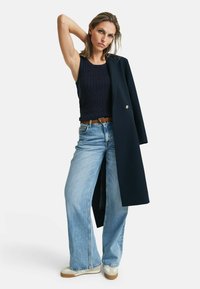 Marineblauw geribbelde tanktop, brede lichtblauwe jeans en een lange marineblauwe jas met een gouden knoop. Afgerond met witte sneakers en een bruine riem.