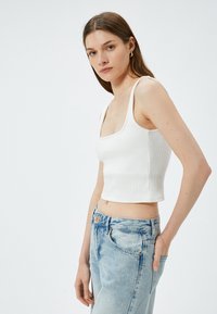 Witte geribde crop top met vierkante halslijn, gedragen met lichtblauwe hoge taille jeans. De top heeft dikke bandjes en een getailleerd ontwerp.