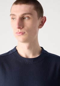 Námořnická modrá tričko s kulatým výstřihem z hladkého bavlněného materiálu, s jemně embosovaným logem "BOSS" na límci a minimálními detaily šití.