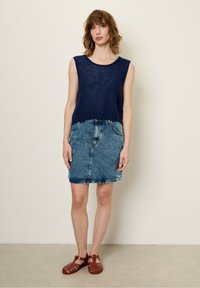 Granatowa, bezrękawnikowa bluzka dzianinowa skomponowana z jasnoniebieską dżinsową spódnicą i brązowymi sandałami na paski. Bluzka jest lekko skrócona i luźna.