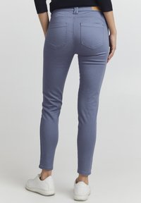 Slim-fit džíny ve světle šedé barvě s hladkou texturou, obsahující dvě zadní kapsy a středně vysoký pas, kombinované s bílými teniskami.