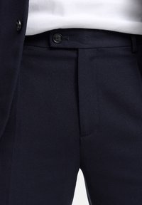 Ciemnogranatowe spodnie wykonane z fakturowanej tkaniny, z płaskim przodem, szlufkami na pasek, pojedynczym guzikiem oraz bocznymi kieszeniami.