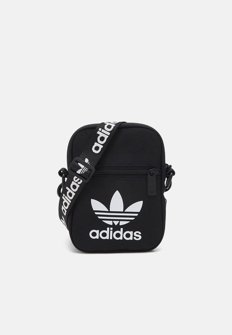 Černá látková crossbody taška s bílým logem Adidas, se zipovým uzávěrem, nastavitelným popruhem a obdélníkovým tvarem.