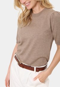 Pletený khaki top s krátkým rukávem a kulatým výstřihem, doplněný o detail nabraných ramen, v kombinaci s bílými kalhotami s vysokým pasem a hnědým opaskem.