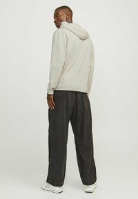 Haut à capuche gris clair avec une coupe oversize et une capuche, associé à un pantalon noir ample. Il présente un design minimaliste et une texture lisse.